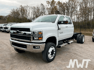 White Chevrolet truck on a gravel lot with trees in the background