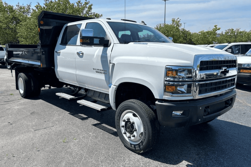 A white Chevrolet Silverado 5500HD dump truck with a black dump bed parked in an outdoor parking lot on a sunny day.