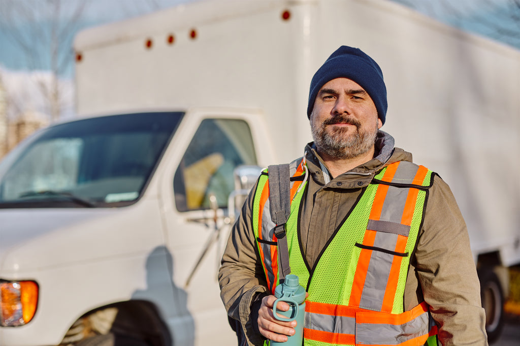 Man in safety vest and beanie standing in front of a truck